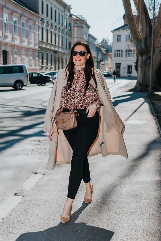 Modebloggerin Miss Classy trägt ein Outfit mit Trenchcoat von Guess, einer schwarzen Skinny Jeans, einer gemusterten Bluse und Pumps. Als Accessoires trägt sie einen Gürtel von Gucci mit Doppel G Schnalle und die Gucci Marmont Schultertasche.