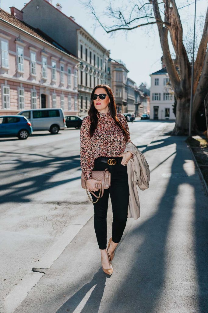 Modebloggerin Miss Classy trägt ein Outfit mit Trenchcoat von Guess, einer schwarzen Skinny Jeans, einer gemusterten Bluse und Pumps. Als Accessoires trägt sie einen Gürtel von Gucci mit Doppel G Schnalle und die Gucci Marmont Schultertasche.