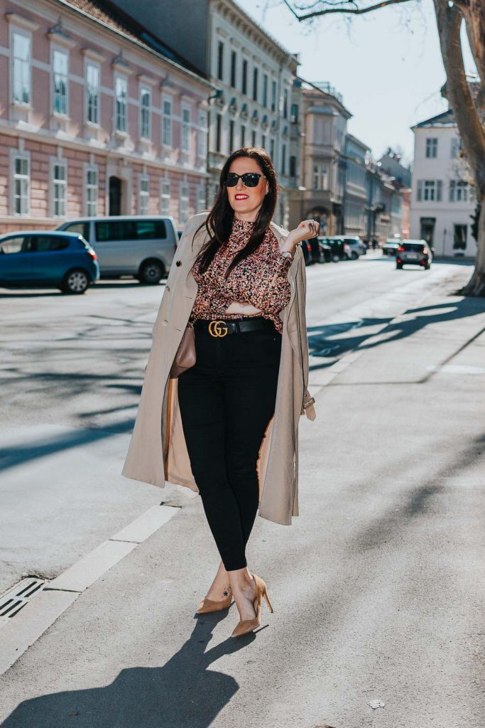 Modebloggerin Miss Classy trägt ein Outfit mit Trenchcoat von Guess, einer schwarzen Skinny Jeans, einer gemusterten Bluse und Pumps. Als Accessoires trägt sie einen Gürtel von Gucci mit Doppel G Schnalle und die Gucci Marmont Schultertasche.